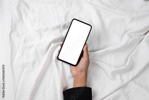 Hand holding smartphone with blank white screen on bed