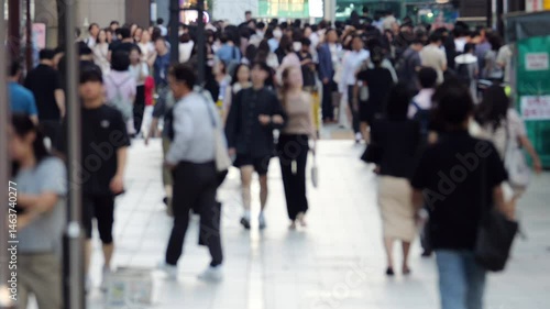 Blurred view of pedestrian crowd walking along bustling sidewalk at Gangnam area, vibrant urban flow as office workers leave for home, typical end-of-day scene in busy South Korean metropolis.