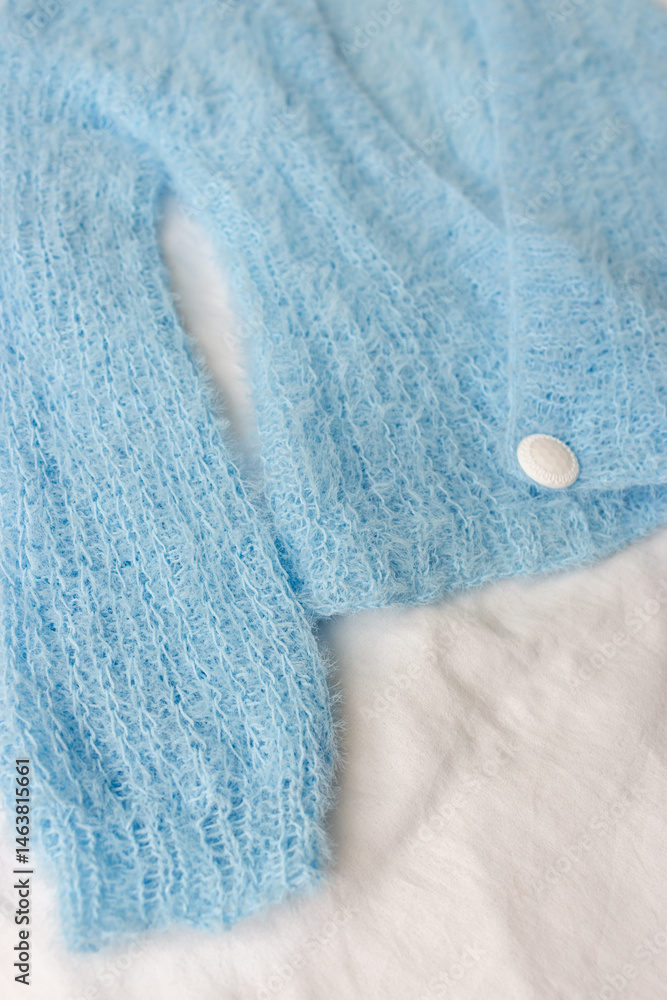Blue knitted cardigan with white button on white background. Soft blue knitted sweater in details. Knitting pattern background. Summer knitted fashion. Cozy hobby. Craft product concept.