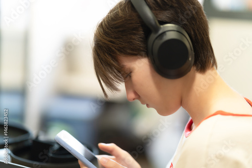 Fotografie Side view of a teen in headphones focused on a smartphone