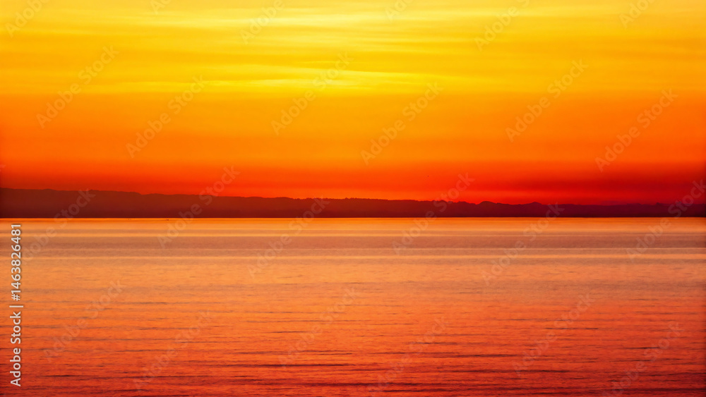 Fototapeta premium Vibrant Sunset Over Calm Ocean Waves with Beautiful Orange and Yellow Sky Colors