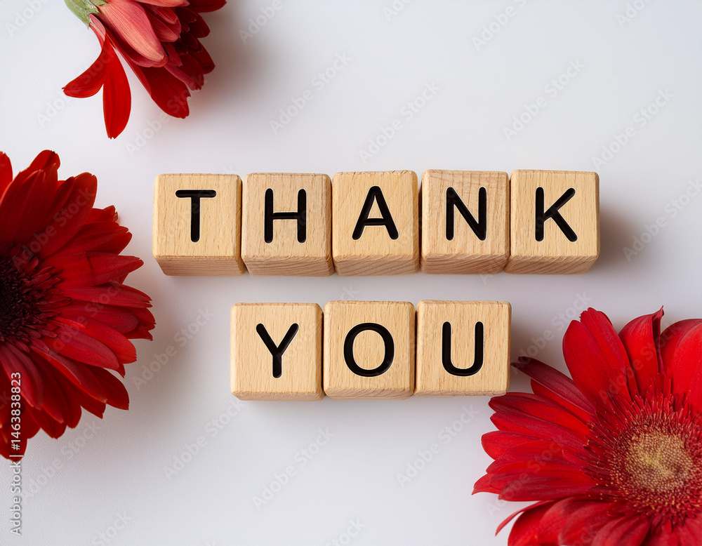 The word THANK YOU written in wooden cubes on a white background with some flowers