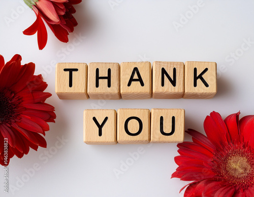 The word THANK YOU written in wooden cubes on a white background with some flowers