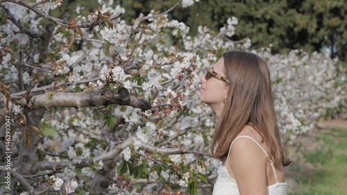 Beautiful woman gently touches and smells blooming pink flowers on a spring peach or sakura tree branch, close-up. A serene moment of connection with nature, beauty, and femininity