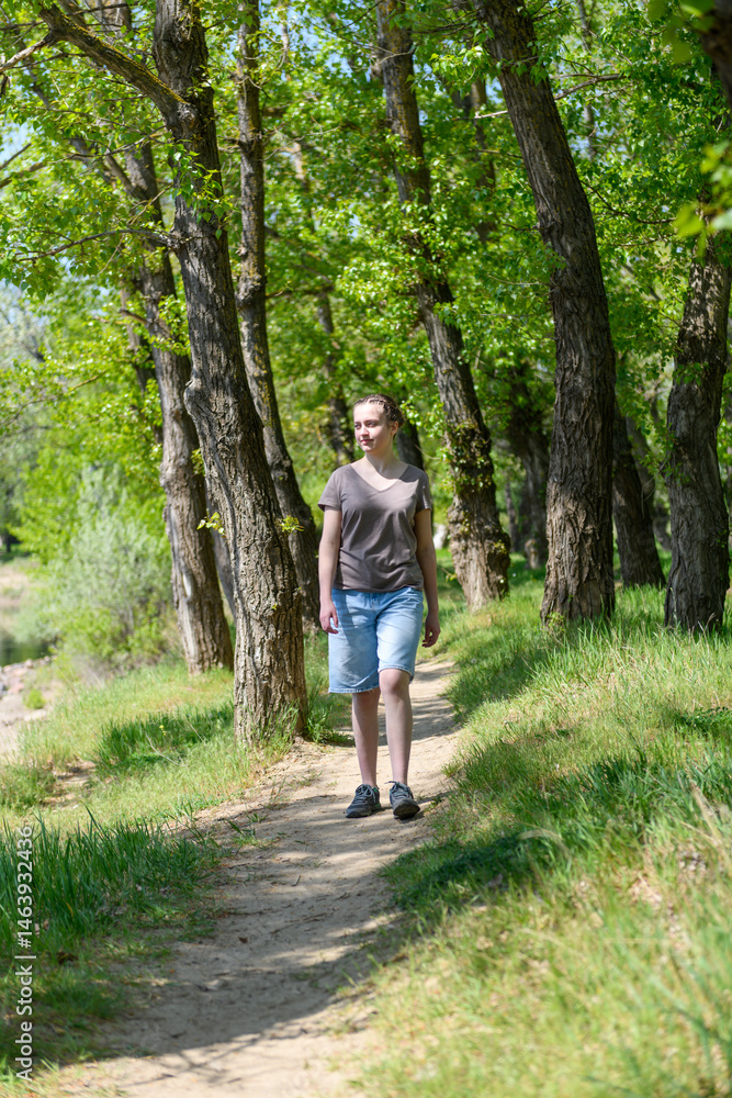 Obraz premium Teen girl a girl walks along a forest path, beautiful spring nature, green leaves, landscape