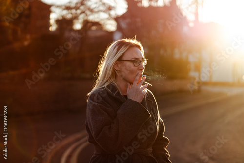 Obraz na plátně A woman with blonde hair smokes a cigarette at sunset