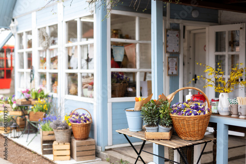 Wallpaper Mural Showcase street market with flowers and plants. Table on terrace for sale laurel in pots and gardening tools. Facade сozy coffee shop with garden furniture. Gardening hobby at home concept Torontodigital.ca