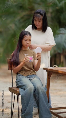 Asian mother braids her daughter's hair