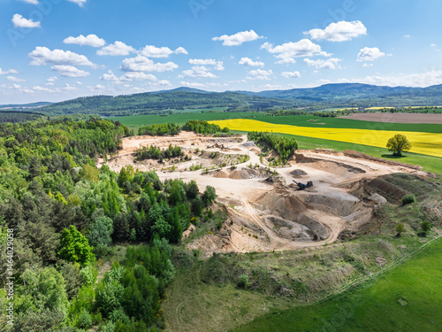 Obraz na płótnie Aerial drone view of sand or gravel quarry surrounded by forest and farmland with distant hills. Aerial Drone view shows an inactive or abandoned quarry embedded in a green landscape. w salonie