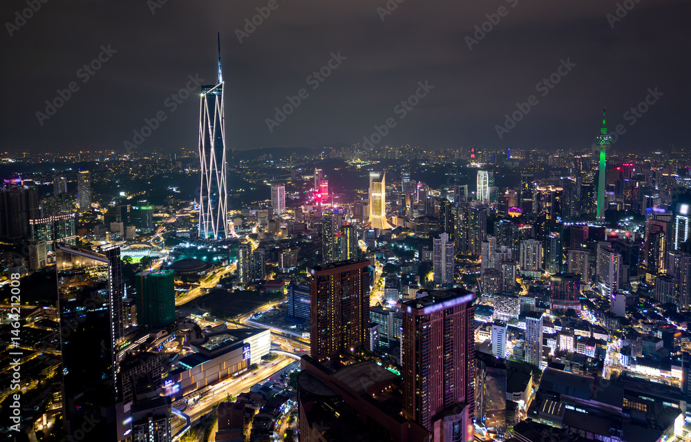 Obraz premium Aerial view of Kuala Lumpur city skyline at night with glowing skyscrapers and illuminated roads
