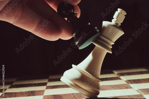 Black pawn knocking down white king on chessboard
