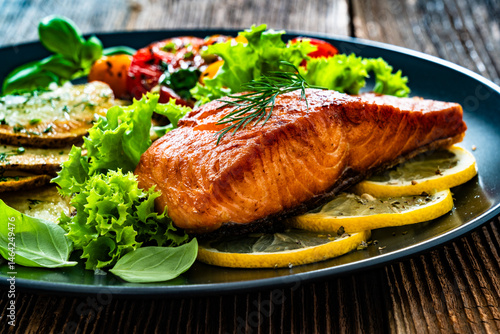 Seared salmon steak with cherry tomato salad and fried potato slices on wooden table	