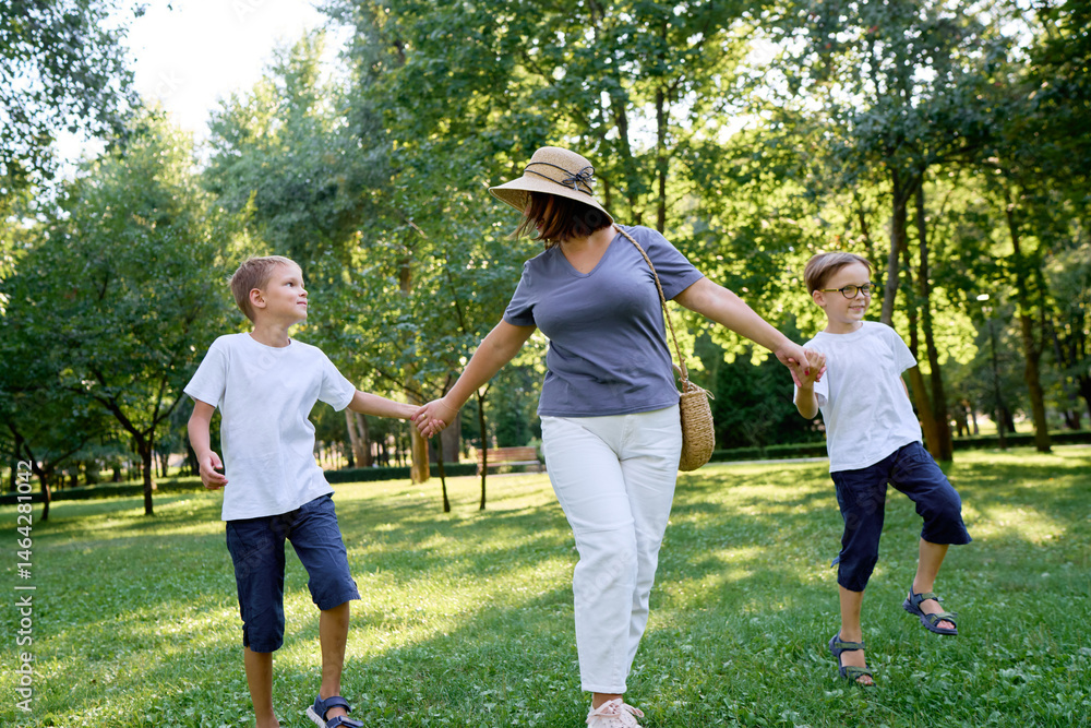 Obraz premium Mother Walking in Park With Two Sons Enjoying a Bright Sunny Day..