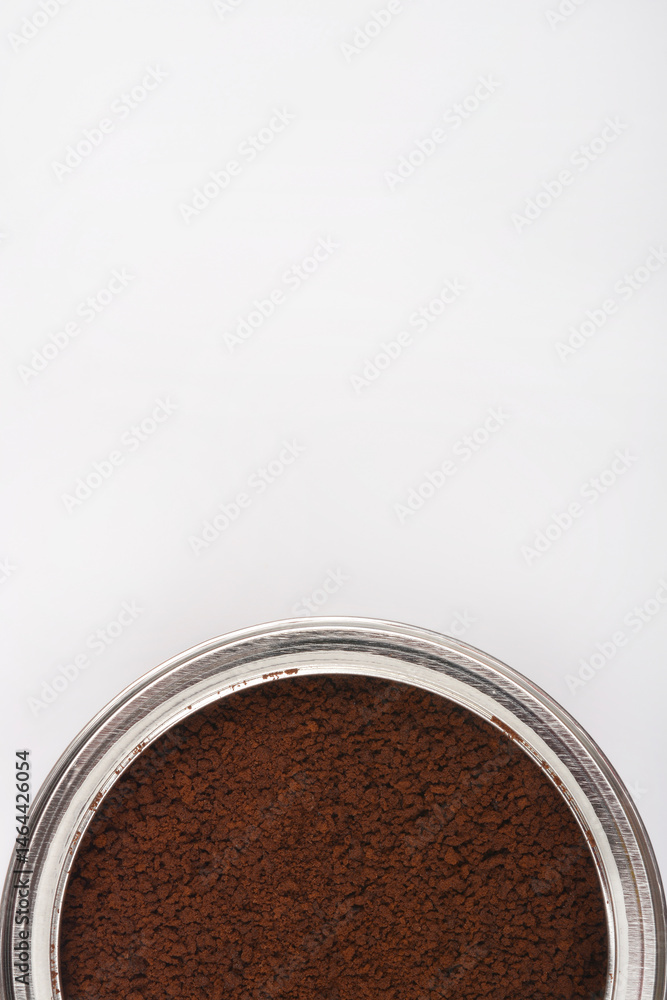 A close-up shot shows a silver rimmed container filled with dark brown instant coffee granules against a bright white background