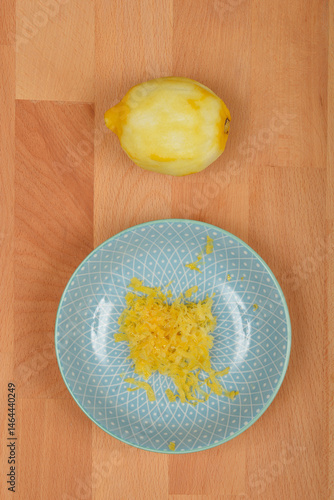 Obraz na płótnie A peeled lemon sits above a light blue decorative plate containing freshly grated yellow lemon zest, all on a light brown wooden surface w salonie