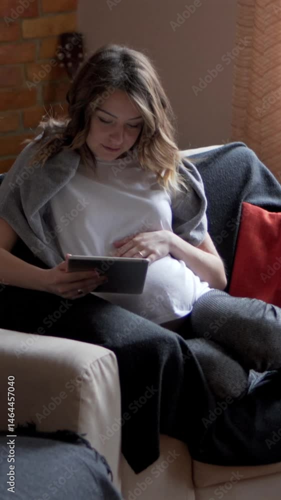 Smiling pregnant woman browses the internet using a tablet pc at home, enjoying leisure and communication during free time. Vertical video. Smiling pregnant woman browses the internet using a tablet pc at home, enjoying leisure and communication during free time. Vertical video.