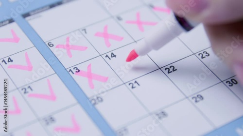 Hand marking pink checkmarks on a calendar, representing planning and tracking.