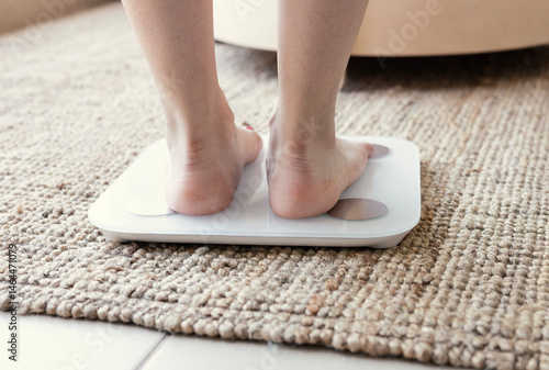 Young woman standing on scales at home, close up. Weight loss concept	