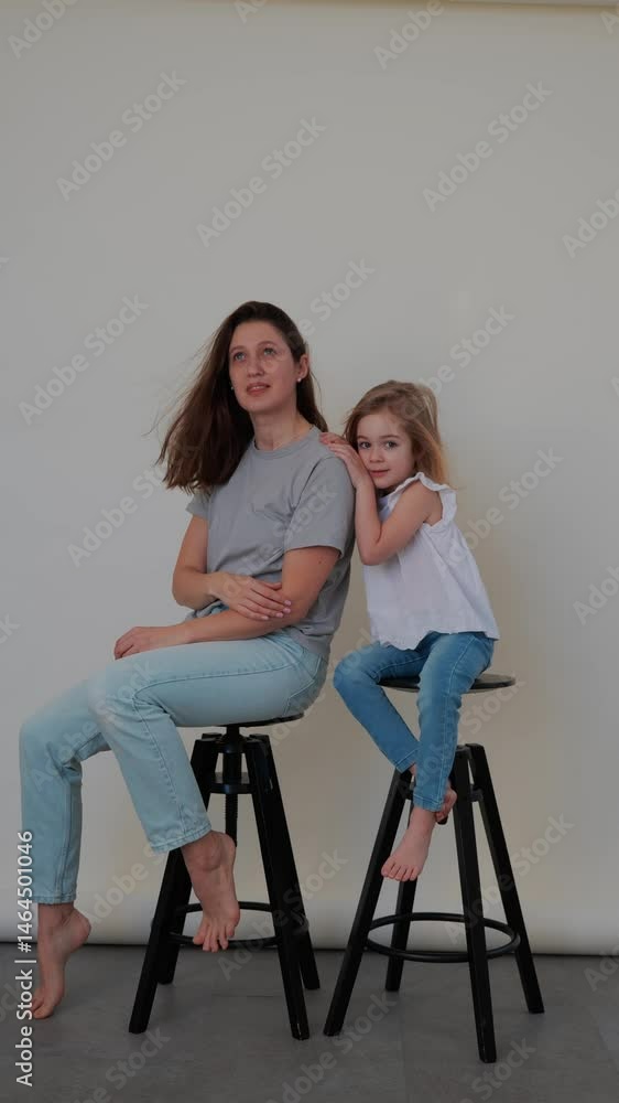 Mom and daughter share a joyful moment while sitting on stools during a casual indoor session Mom and daughter share a joyful moment while sitting on stools during a casual indoor session