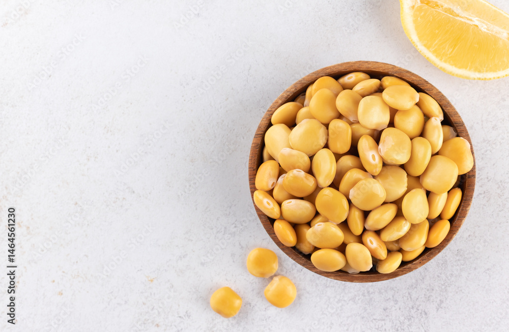 Pickled lupini beans in a wooden plate with lemon on a gray background. Top view. Copy space. Plant protein. Pickled lupini beans in a wooden plate with lemon on a gray background. Top view. Copy space. Plant protein.