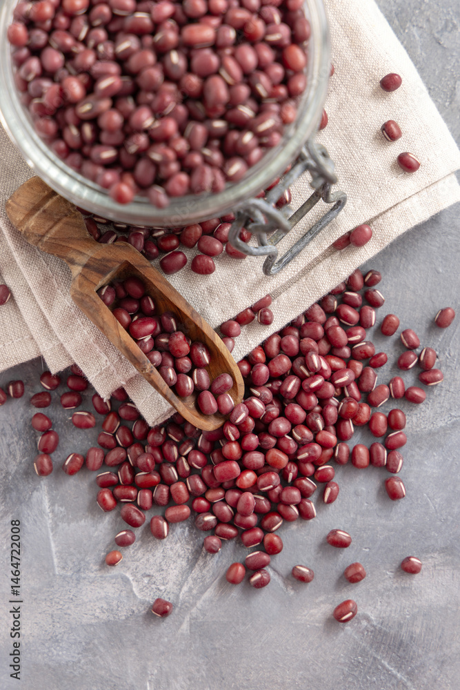 Glass jar full of dried azuki beans with a wooden scoop top view. Vegetarian protein source