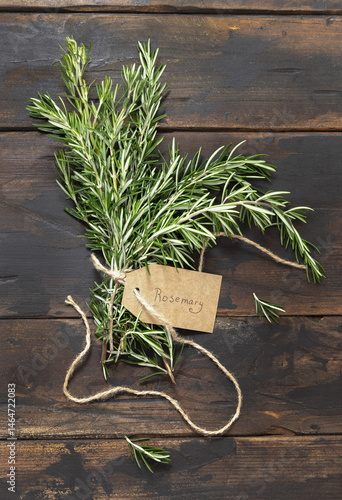 Obraz na płótnie Fresh green rosemary sprigs with kraft paper text label dark weathered wooden table top view w salonie