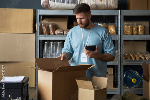 Foto Man standing in warehouse while packing food items into cardboard boxes for shipment
