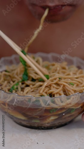 Delicious chicken noodle culinary food. Close up view of male hand stirring chicken noodles in a glass bowl with chopsticks. Ready to eat. Vertical video 4K.