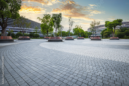 Empty brick paved plaza with trees and modern buildings in a business park area at dusk.