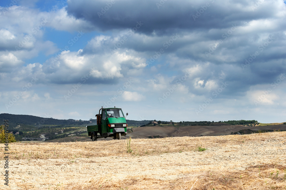 Fototapeta premium Small three-wheeler on the Sienese hills among the fields after the harvest