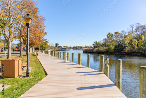 Fotografie Empty boardwalk lined with trees and wooden benches and lamp posts on a river harbour on a clear autumn morning