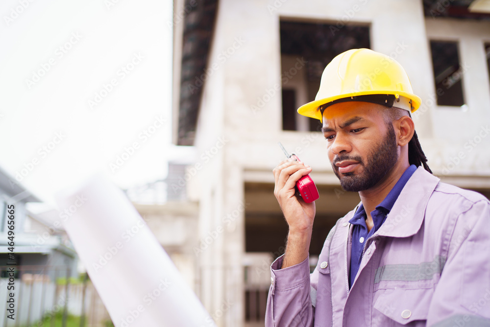 Hispanic male engineer holding blueprints at a construction site, reviewing housing project progress. Hispanic male engineer holding blueprints at a construction site, reviewing housing project progress.
