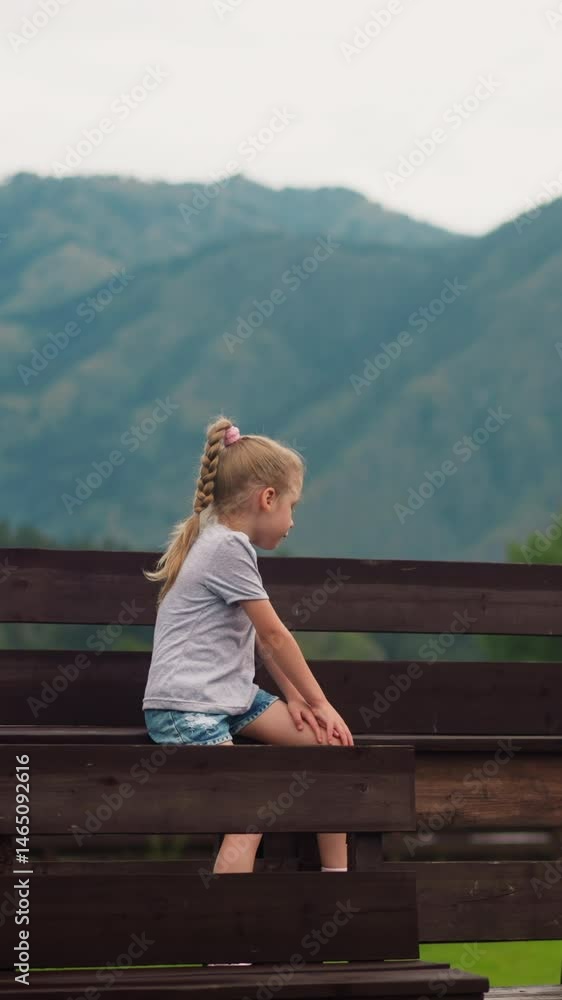 Cute little boy with wild flowers bouquet looks at distant mountains while girl sister sits on wet wooden bench at resort hotel on nasty day Cute little boy with wild flowers bouquet looks at distant mountains while girl sister sits on wet wooden bench at resort hotel on nasty day