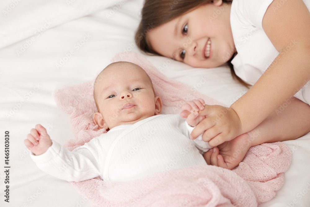 Cute girl and her little sister on bed at home, selective focus Cute girl and her little sister on bed at home, selective focus