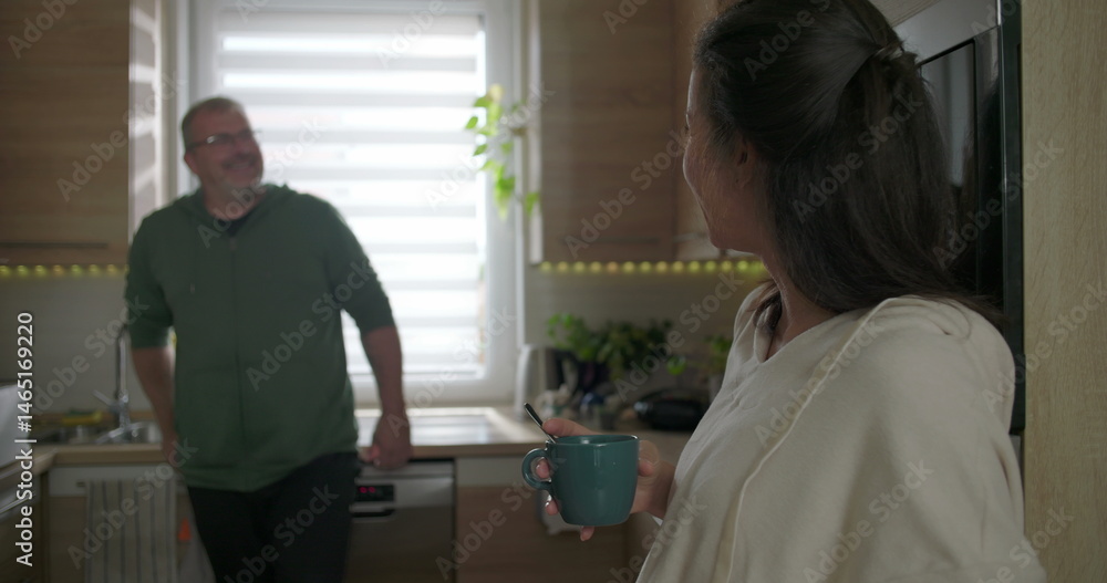 Two adults having a light-hearted conversation in a modern kitchen, woman holding a blue mug and smiling while stirring, man leaning against the counter, relaxed atmosphere Two adults having a light-hearted conversation in a modern kitchen, woman holding a blue mug and smiling while stirring, man leaning against the counter, relaxed atmosphere