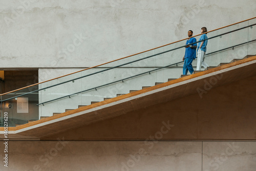 Full length of multiracial male and female nurse talking with each other while moving down steps of hospital building