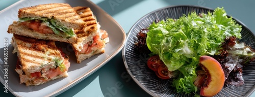 Tasty sandwich featuring avocado served with fresh peach slices and a side salad, all elegantly displayed on a blue plate.
