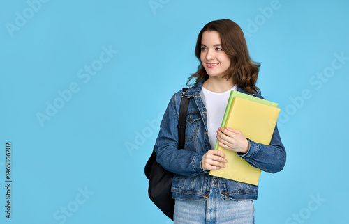 Pretty student girl holding notebooks and looking away, isolated on blue background.
