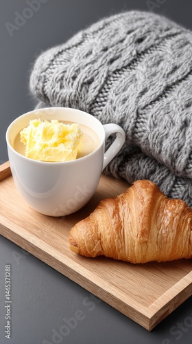 Softly lit close-up of a croissant with butter and coffee on a wooden tray, creating a warm morning atmosphere