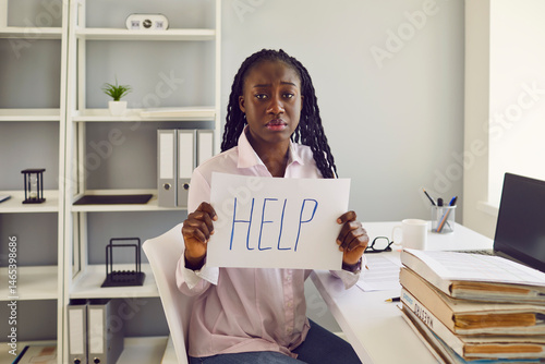 Obraz na plátně African American woman office worker sits at desk with paperwork and laptop, loo