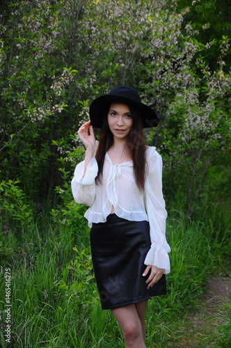 young girl walking in a summer park in a black hat in a white blouse and skirt