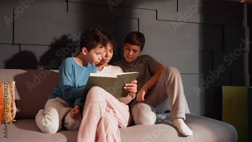 A 25-year-old Latina sister with mid-length, curly brunette hair, sitting on the sofa at home wearing cozy clothes, holding a book as her two kid brothers sit beside her, reading it together