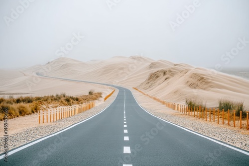 Wide Road Bordered by Drifting Sand Dunes Showcases a Serene Landscape During Foggy Weather