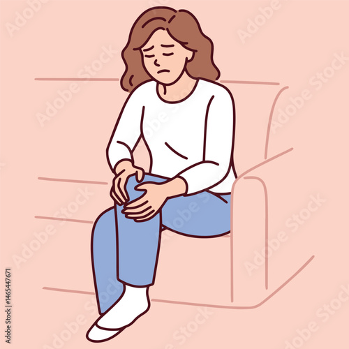 Woman sitting on couch holding knee in pain possibly due to joint inflammation or muscle strain