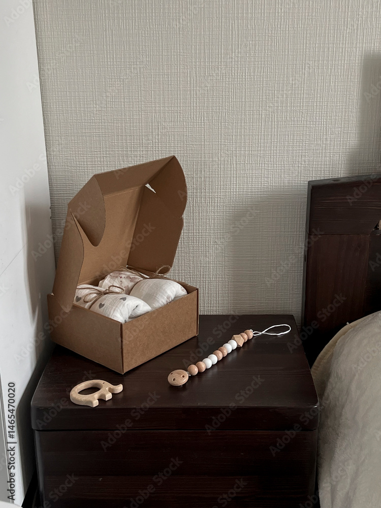 A box of muslin diapers, beads, and a wooden elephant teether are on the bedside table. Fashionable Scandinavian accessories for newborns on the bedside table