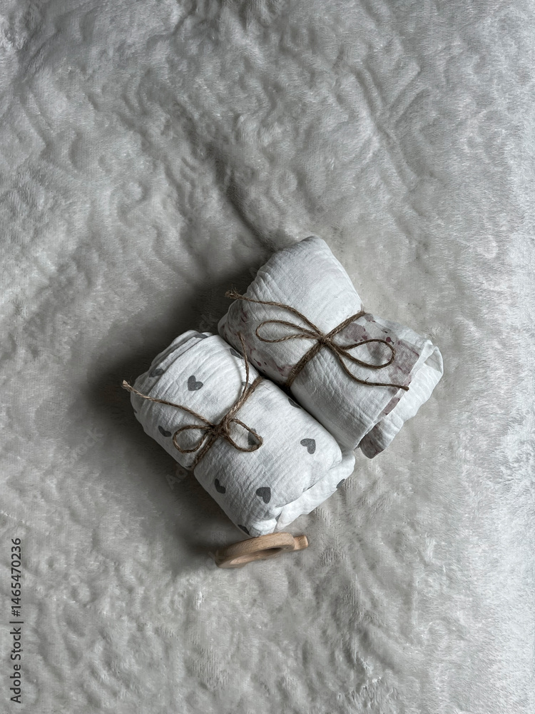 Two twisted muslin diapers and an elephant teether are lying on a milky-colored blanket. Children's fashion accessories