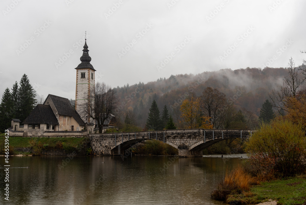 St. John the baptist's church rising from bohinj lake embankment on cloudy autumn day