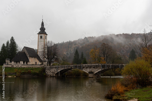 Obraz na płótnie St. John the baptist's church rising from bohinj lake embankment on cloudy autumn day w salonie
