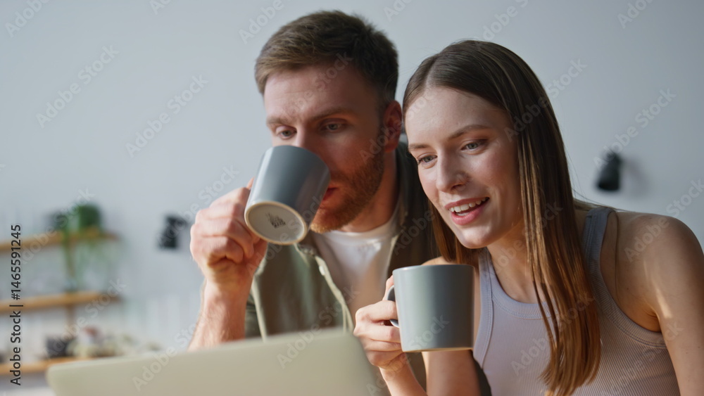 Lovely pair drinking coffee looking laptop in kitchen closeup. Happy man woman