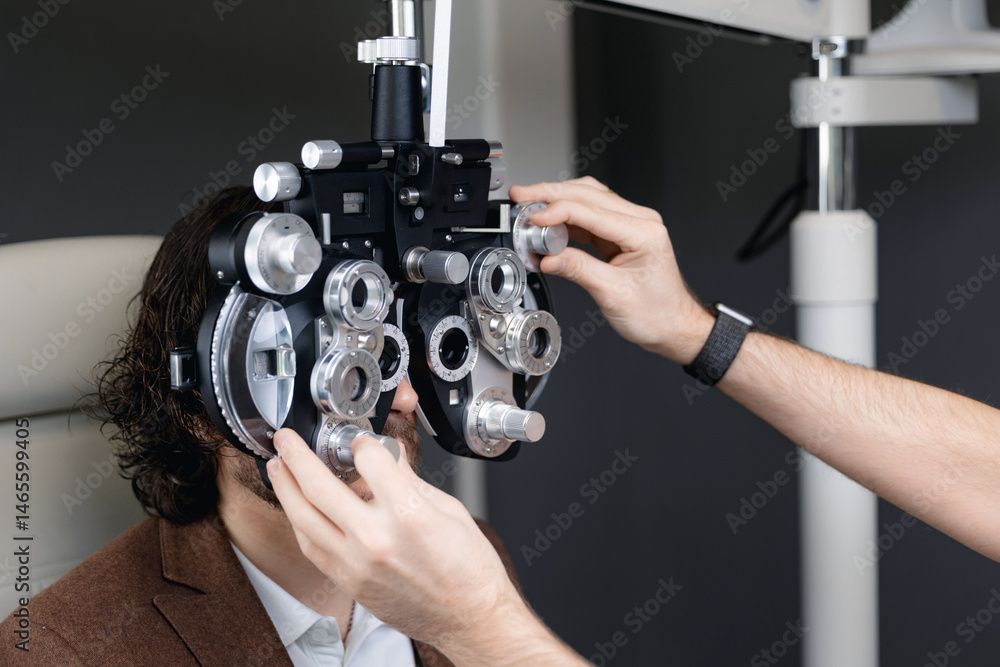 Male patient undergoing eye exam with optometrist using phoropter in clinic